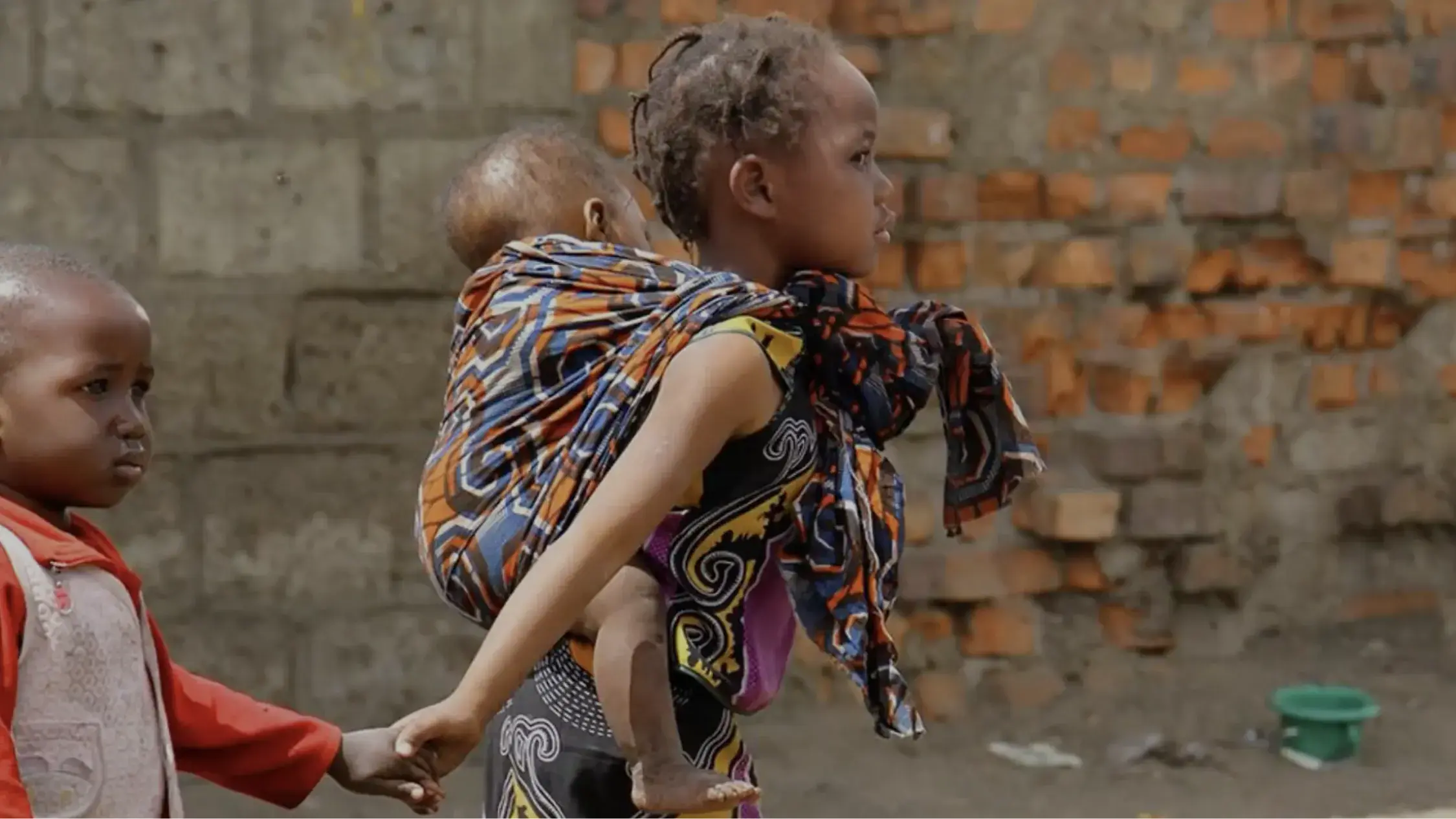 Child with colorful scarf smiling and walking with baby on back