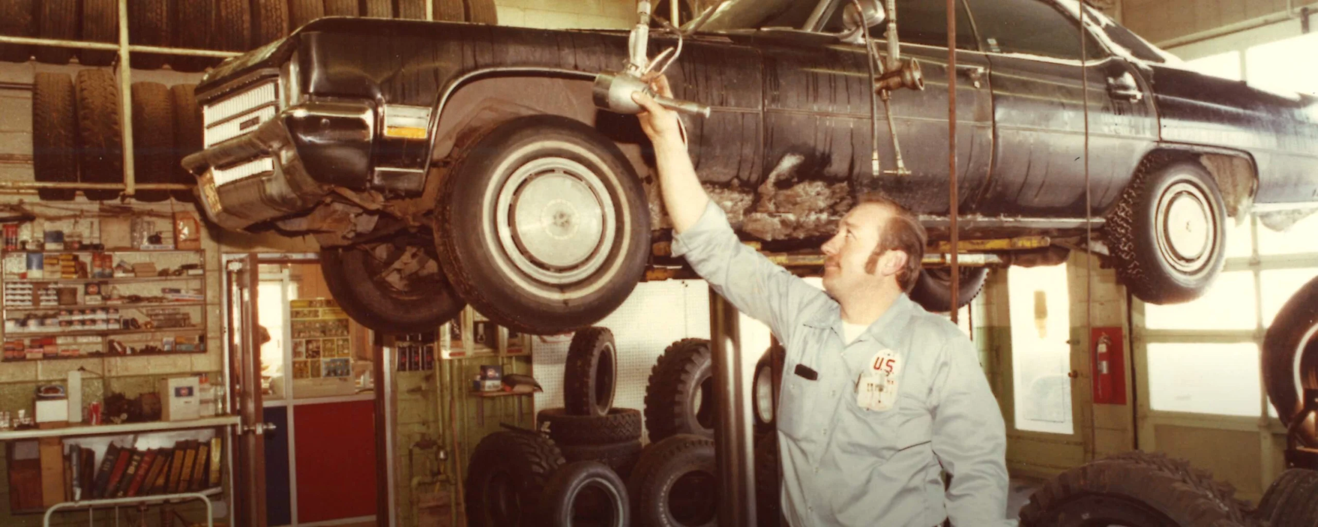 Historic photo of automotive technician repairing truck undercarriage in service garage
