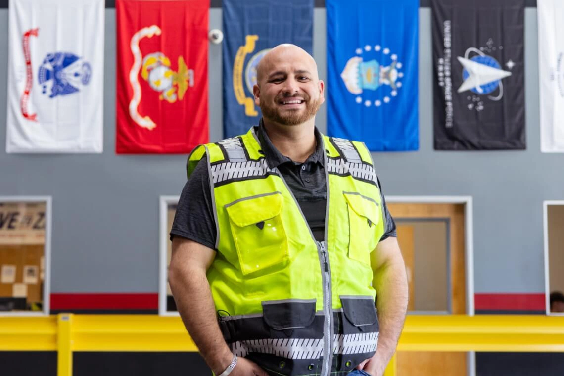 U.S. Venture team member in safety vest in front of service branch flags